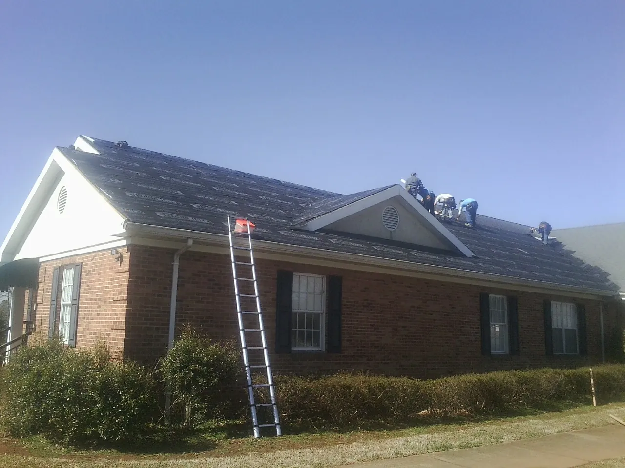 Crew tearing shingles off a brick ranch roof with a ladder set — Metal Roof Repair work by our crew in Prospect
