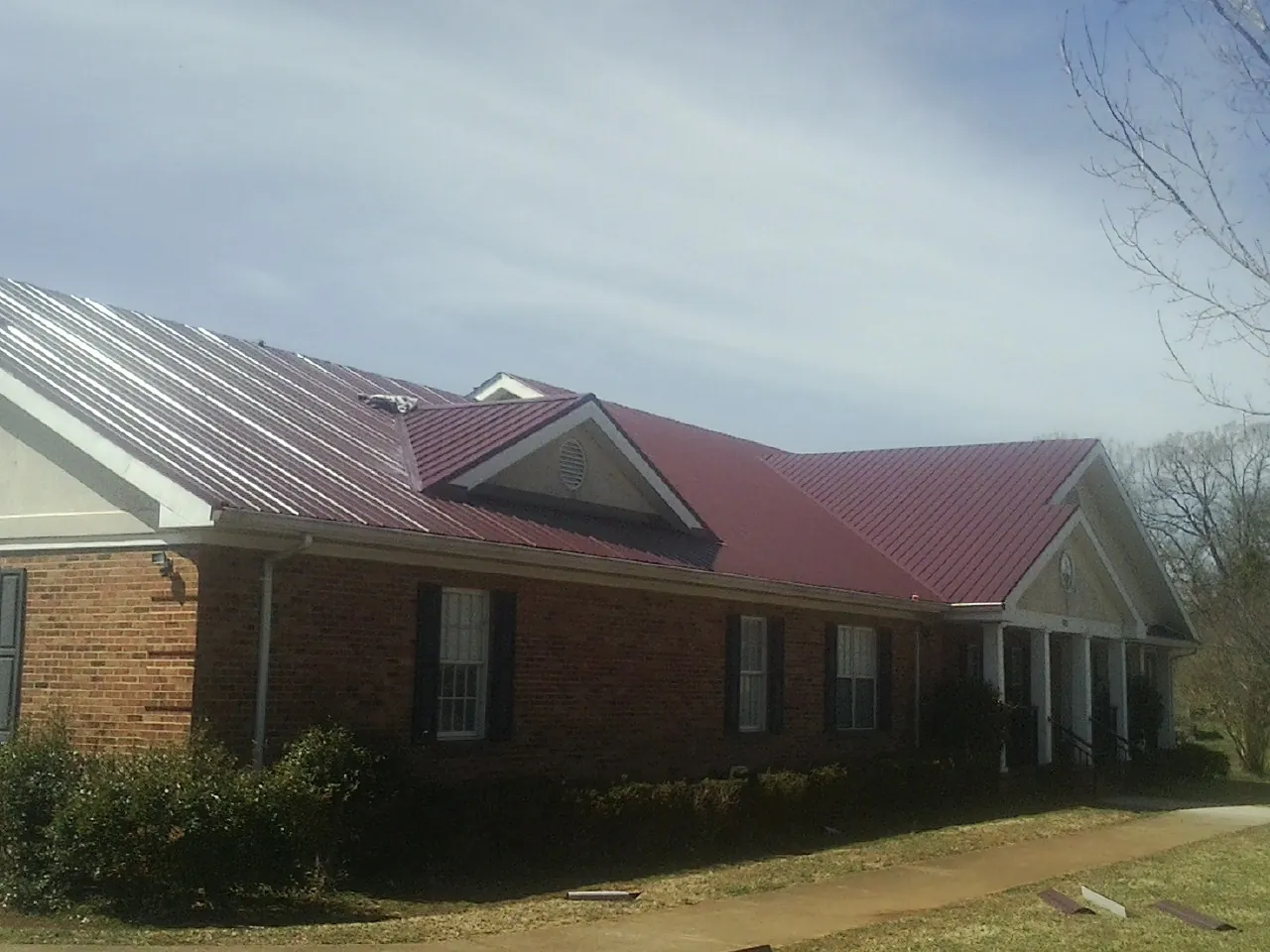 Red metal roof with gabled entries on a long brick building, from a Hail Damage Roof Repair job in Prospect