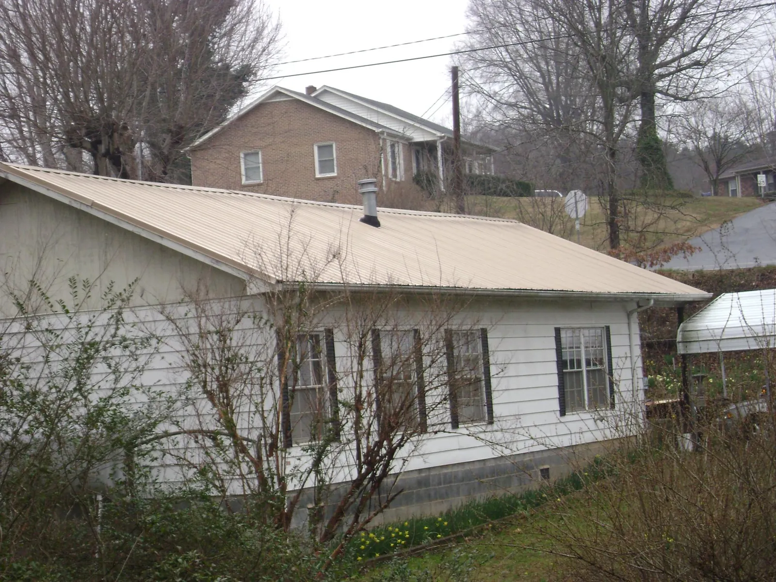 Tan metal roof on a white sided house set into a hillside — Commercial Roofing by Roofing Brothers in Prospect